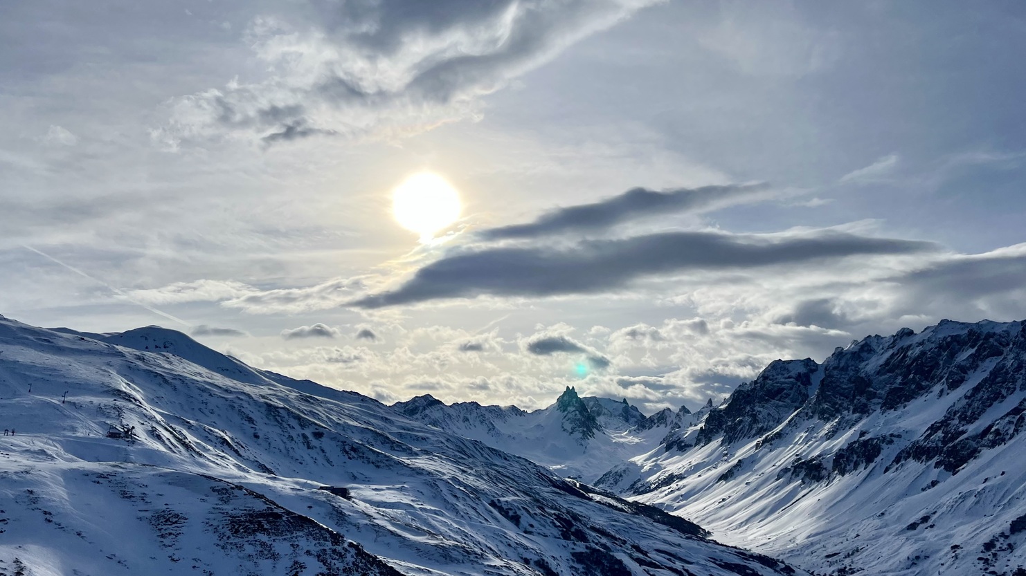 Schneebedeckte Berge mit der Sonne und Wolken am Himmel, der eine alpine Landschaft im Winter darstellt.