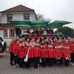 Gruppe von M&auml;dchen in roten Jacken posiert vor einem Wagen mit Sonnenschirmen und einem Geb&auml;ude im Hintergrund.