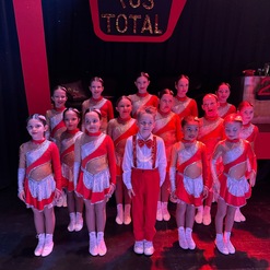 Gruppe von Kindern in roten Kost&uuml;men mit Glitzer, stehen vor schwarzem Hintergrund mit &bdquo;TUS TOTAL&ldquo; Schriftzug.