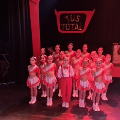 Gruppe von jungen T&auml;nzern in roten und silbernen Kost&uuml;men, posiert auf der B&uuml;hne vor einem "TUS TOTAL"-Schild.