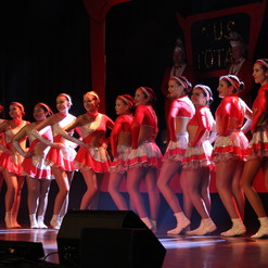 Gruppe von T&auml;nzerinnen in roten Kost&uuml;men posiert auf der B&uuml;hne bei einer Auff&uuml;hrung.