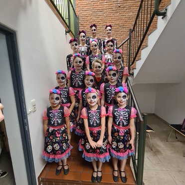 Gruppierung von M&auml;dchen mit Totenkopf-Make-up und festlichen Kleidern, die auf einer Treppe posieren.