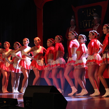 Gruppe von T&auml;nzerinnen in roten Kost&uuml;men posiert auf der B&uuml;hne bei einer Auff&uuml;hrung.