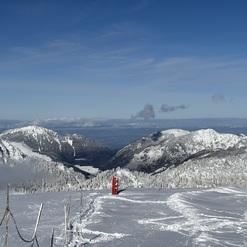 Schneebedeckte Berge unter blauem Himmel mit rotem Orientierungsschild im Vordergrund, umgeben von schneeigen Landschaften.