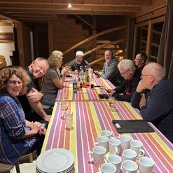 Geselliges Beisammensein am Tisch mit verschiedenen Personen, Getränken und Geschirr in einer holzverkleideten Umgebung.