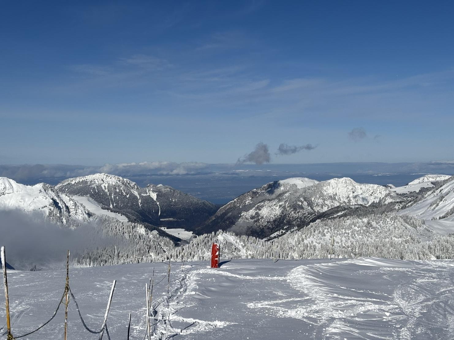 Schneebedeckte Berge unter blauem Himmel mit rotem Orientierungsschild im Vordergrund, umgeben von schneeigen Landschaften.