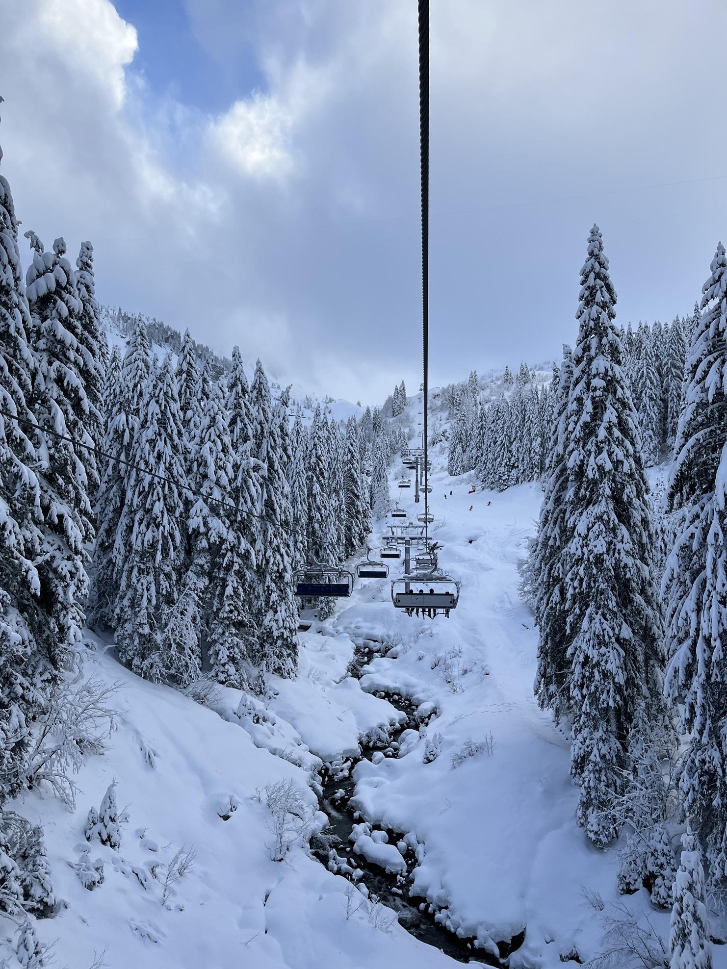Seilbahn über schneebedeckte Bäume und einen zugefrorenen Bach in winterlicher Berglandschaft.
