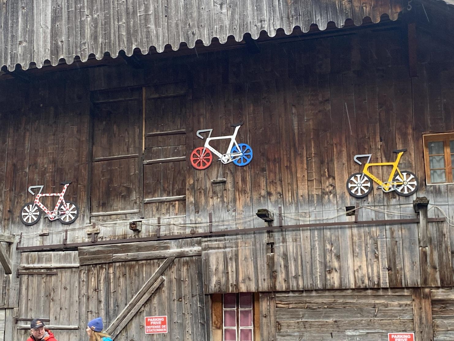Bunte Fahrrad-Motive an einer rustikalen Holzwand mit Fenstern und Hinweisschildern.