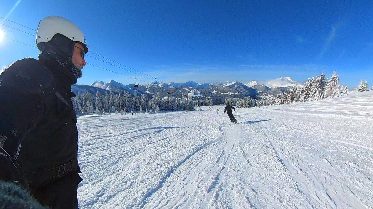 Skifahrer fährt eine verschneite Piste mit Bergpanorama und blauen Himmel im Hintergrund.
