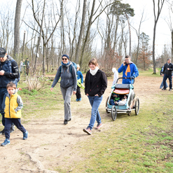 Gruppe von Erwachsenen und Kindern spaziert auf einem schmalen Weg durch einen bewaldeten Park im Frühling.