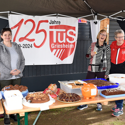 Drei Frauen stehen an einem Tisch mit Kuchen und Snacks, im Hintergrund ein Banner zum 125-jährigen Jubiläum des TuS Griesheim.