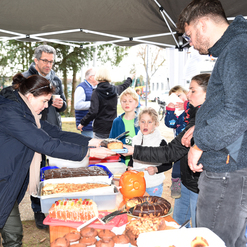 Lebhafte Szene an einem Stand mit verschiedenen Kuchen und Gebäck, während Erwachsene und Kinder miteinander interagieren.