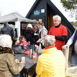 Gruppierung von Menschen am Tisch, die snacks genießen und sich unterhalten, vor einem Sportclubgebäude im Freien.