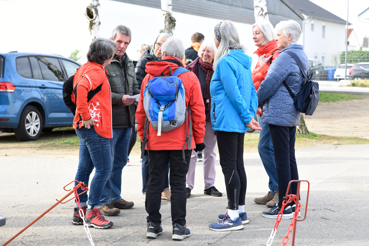 Gruppe von acht Menschen in sportlicher Kleidung steht im Gespräch auf einem Weg, umgeben von Bäumen und Autos.