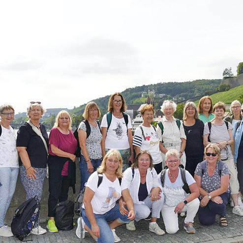 Gruppe von 18 Frauen steht auf einer Brücke mit Blick auf Weinberge und Gebäude im Hintergrund unter bewölktem Himmel.