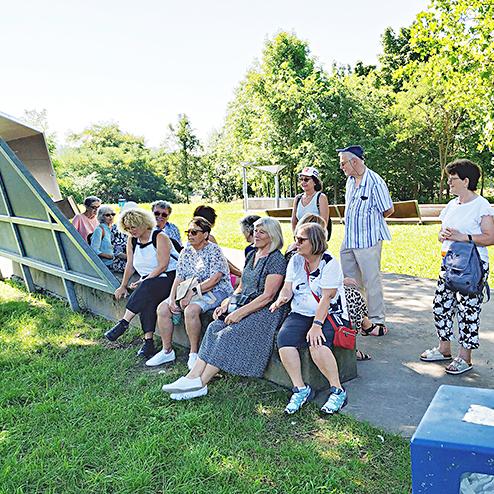 Gruppe von zwölf Personen sitzt auf einer Bank in einer grünen Parklandschaft. Sofortige Eindrücke der Natur.