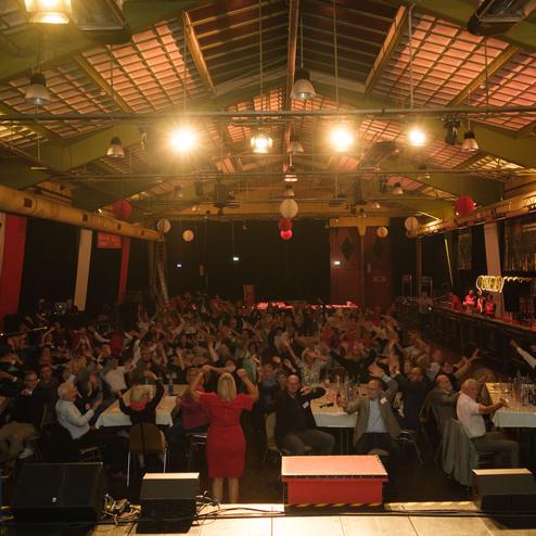 Begeisterte Gäste heben die Hände in einer festlich dekorierten Halle während eines Konzerts.