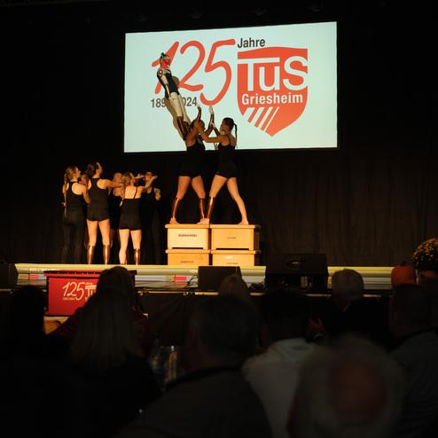 Aufführung mit Mädchen in Schwarz, die auf Kästen tanzen, vor einer großen Leinwand mit dem Logo von TU Griesheim.