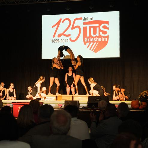 Aufführung von Tänzerinnen in schwarzenoutfits auf der Bühne, mit einer großen Projektionsleinwand im Hintergrund.