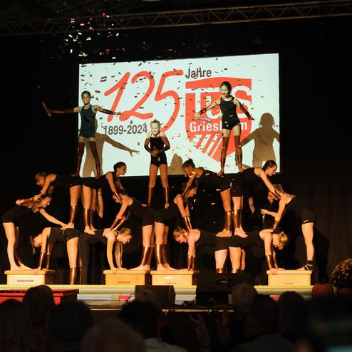 Akrobatik-Performance mit mehreren Tänzern auf Holzpodesten, feierliches Banner zum 125-jährigen Jubiläum im Hintergrund.