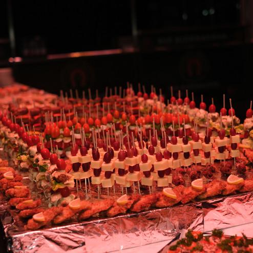 Buffet mit verschiedenen Spießen und Broten, dekoriert mit Gemüse, Käse und frischen Früchten auf einem Tisch.