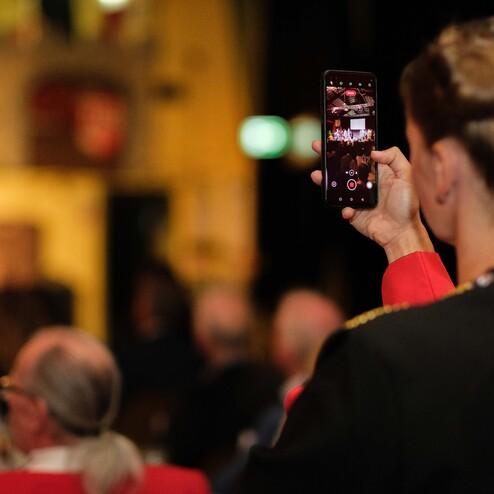 Frau nimmt mit einem Smartphone ein Video von einer Veranstaltung in einem festlichen Raum auf.