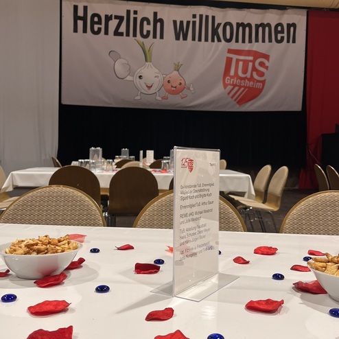 Tisch mit Snacks, Tischschild und dekorativen roten Blütenblättern in einem festlich geschmückten Raum.