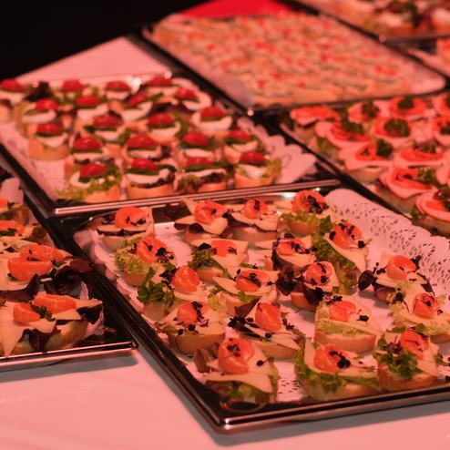 Eingedeckte Tische mit verschiedenen belegten Häppchen auf silbernen Platten, dekoriert mit frischem Gemüse und Kräutern.