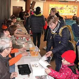 Menschen stehen an einem Tisch, um sich bei einer Veranstaltung anzumelden, während andere helfen und Informationen geben.
