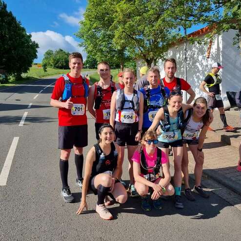 Gruppe von Läufern vor einer Straße, bereit für ein Rennen, mit Startnummern auf ihren Outfits.