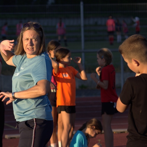 Trainerin gibt Anweisungen an eine Gruppe von Kindern auf einem Sportplatz während eines Trainingsevents.