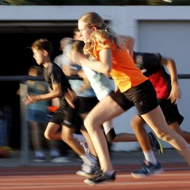 Schnappschuss von Kindern, die sprinten, mit Fokus auf ein Mädchen in orange aus einem dynamischen Lauferlebnis.