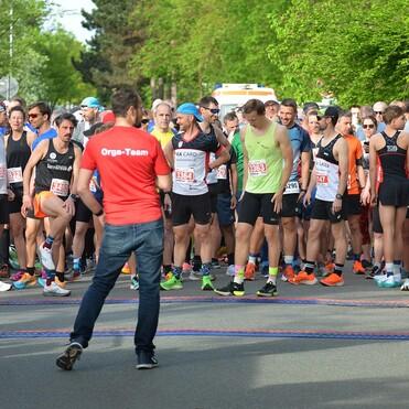 Gruppierung von Teilnehmern an der Startlinie eines Rennens, angeführt von Mitarbeitern des Organisationsteams.