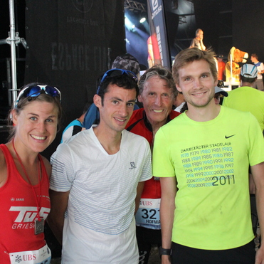 Vier Personen in Sportkleidung lächeln vor einer Bühne mit Veranstaltungshintergrund.