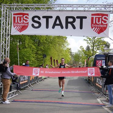 Läufer überquert die Ziellinie beim 50. Griesheimer Jacobi-Straßenlauf unter einem Startbanner.