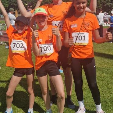 Vier junge Athleten in orangefarbenen T-Shirts posieren fröhlich auf einer Wiese nach einem Wettkampf.