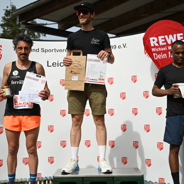 Drei Männer stehen auf dem Siegertreppchen, halten Urkunden und Preise nach einem Sportevent. Hintergrund mit Logos.