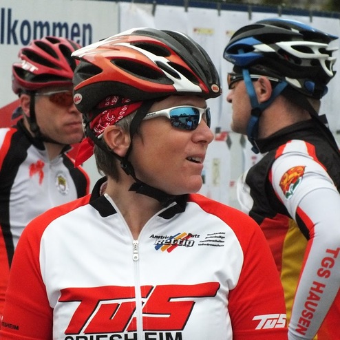 Gruppenszenen von Radfahrern in Trikots, eine Person mit Sonnenbrille und rotem Bandana im Vordergrund.