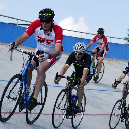 Fünf Radfahrer fahren in Sportkleidung auf einer velodrome-Bahn mit blauer Wand im Hintergrund.