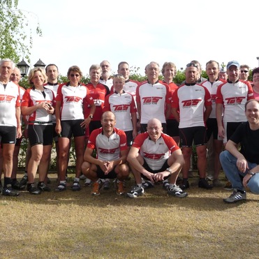 Gruppenfoto von 24 Radfahrern in Trikots mit "TSG Griesheim" Schriftzug, umgeben von grüner Bepflanzung.