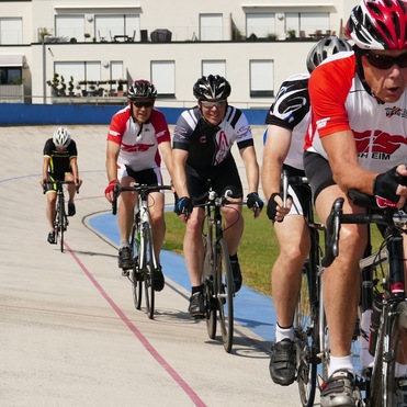 Sechs Radfahrer in Wettkampfkleidung fahren auf einer Radrennbahn mit blauer Umrandung.
