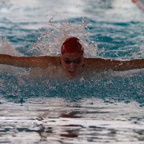 Ein Schwimmer in einem roten Badekappen kämpft sich mit dem Schmetterlingsstil durch das Wasser in einem Schwimmbad.