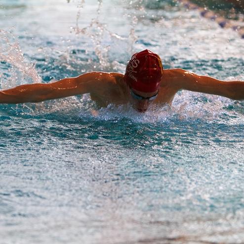 Schwimmer im Wasser, der im Schmetterlingsstil schwimmt, mit Wassertropfen um ihn herum.