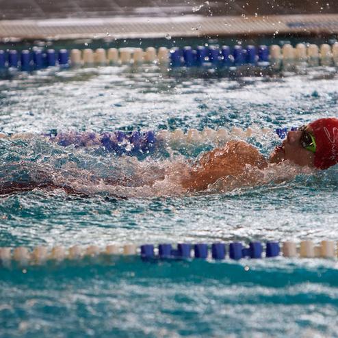 Schwimmer in roter Badekappe und Sonnenbrille, der im Wasser schwimmt, Spritzwasser spritzt um ihn herum.
