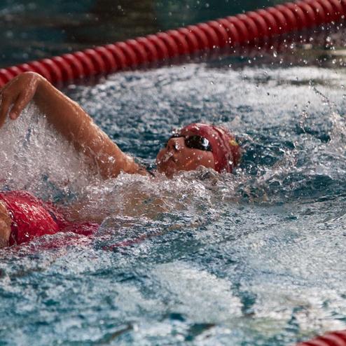 Schwimmerin in rotem Badeanzug und Badekappe vollzieht einen Rückenstil bei Wettkampf im Schwimmbecken.