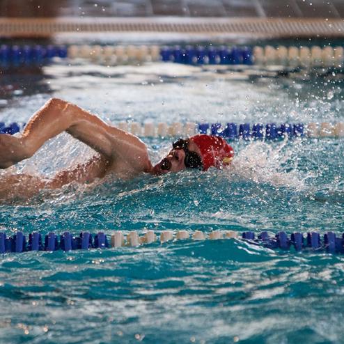 Schwimmer in Action beim Rückenschwimmen im Schwimmbecken, Wasser spritzt um ihn herum.