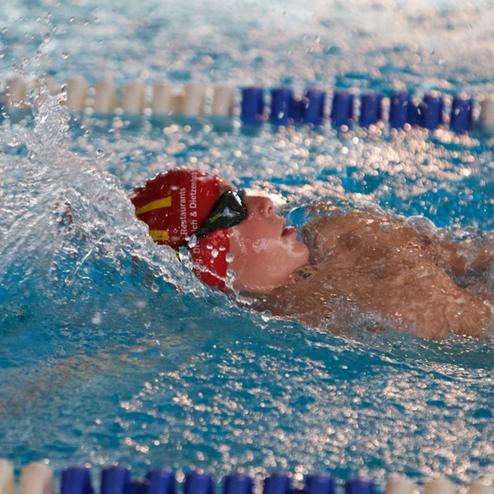 Schwimmer in roten Badekappe und Schwimmbrille im Wasser, während er sich mit kräftigem Armzug vorwärts bewegt.