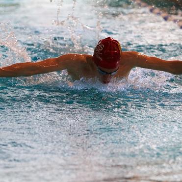 Schwimmer im Wasser, der im Schmetterlingsstil schwimmt, mit Wassertropfen um ihn herum.