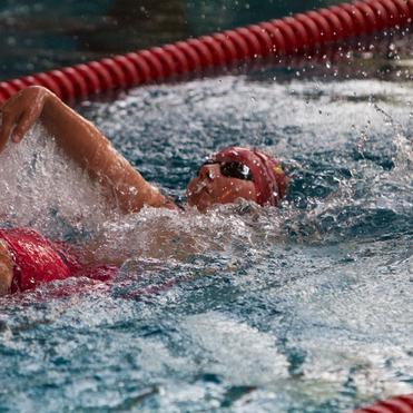 Schwimmerin in rotem Badeanzug und Badekappe vollzieht einen Rückenstil bei Wettkampf im Schwimmbecken.