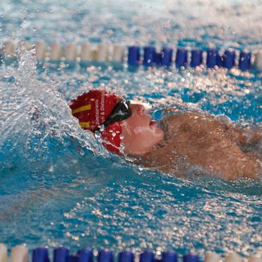 Schwimmer in roten Badekappe und Schwimmbrille im Wasser, während er sich mit kräftigem Armzug vorwärts bewegt.